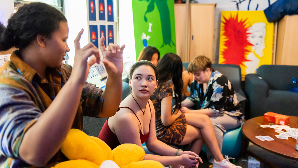 People sit on a couch and exercise ball in a colorful room. Kaylie Cornelius, left, gestures with their hands while Kyna McGill looks on.