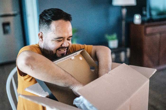 A smiling man opens a cardboard box in his living room