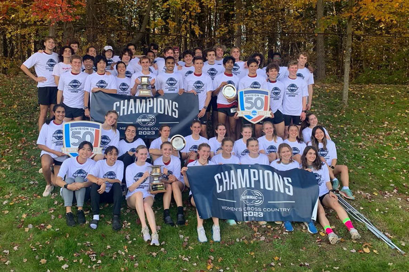 The two cross country teams, about 50 men and women, pose for a group photo with banners that say, "Champions Cross Country 2023"