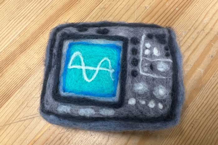 Small, felted oscilloscope has a sine wave on the teal screen