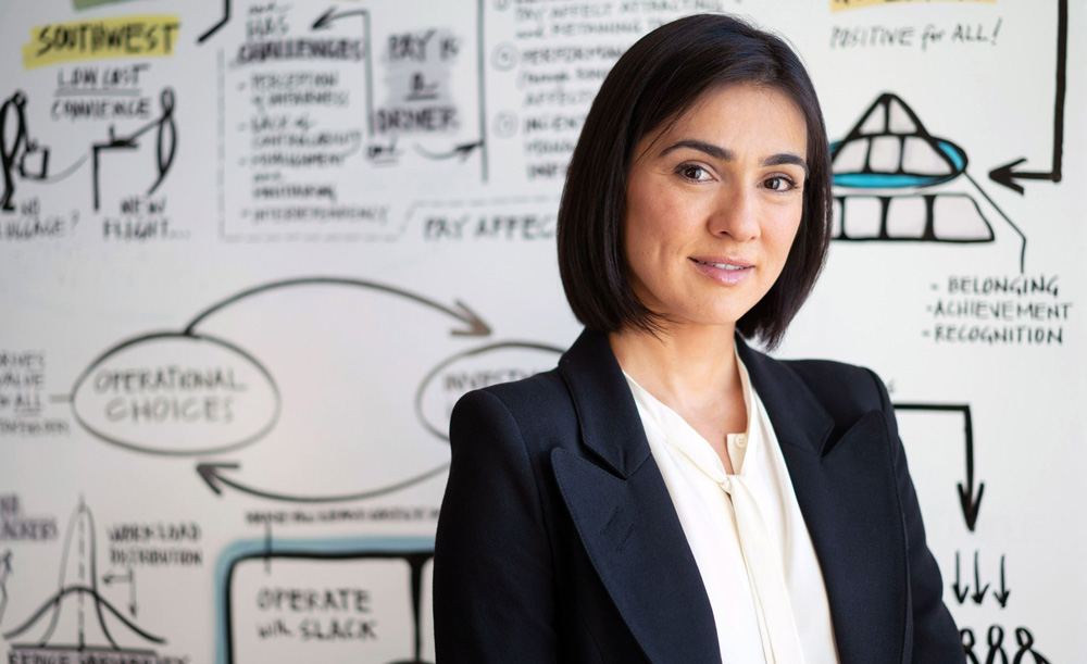 Zeynep ton stands in front of a whiteboard filled with notes and drawings