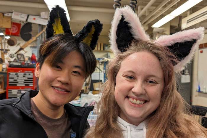 2 students smile while wearing furry animal ears in black and pink