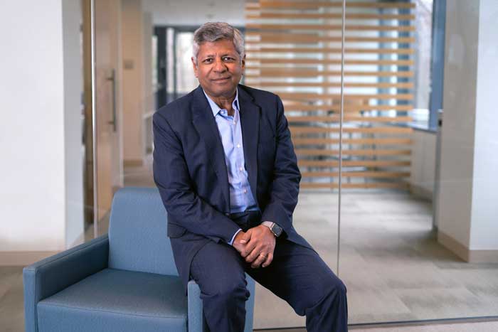 Sudhakar Kesavan sits on side of blue chair in office