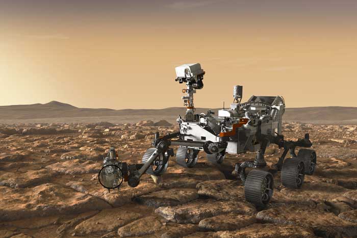 Rendering shows the Perseverance on the rocky brown surface of Mars. The Perseverance resembles a go-cart and has 6 wheels and an arm extending that houses the drill. The top of the Perseverance has a long neck and a camera on top.
