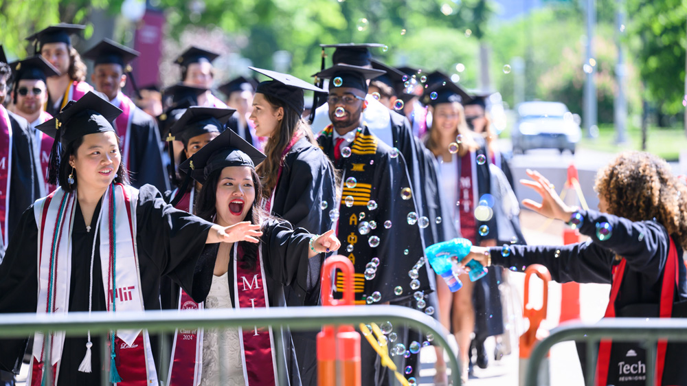 Graduates in a procession react to lots of bubbles a guest makes