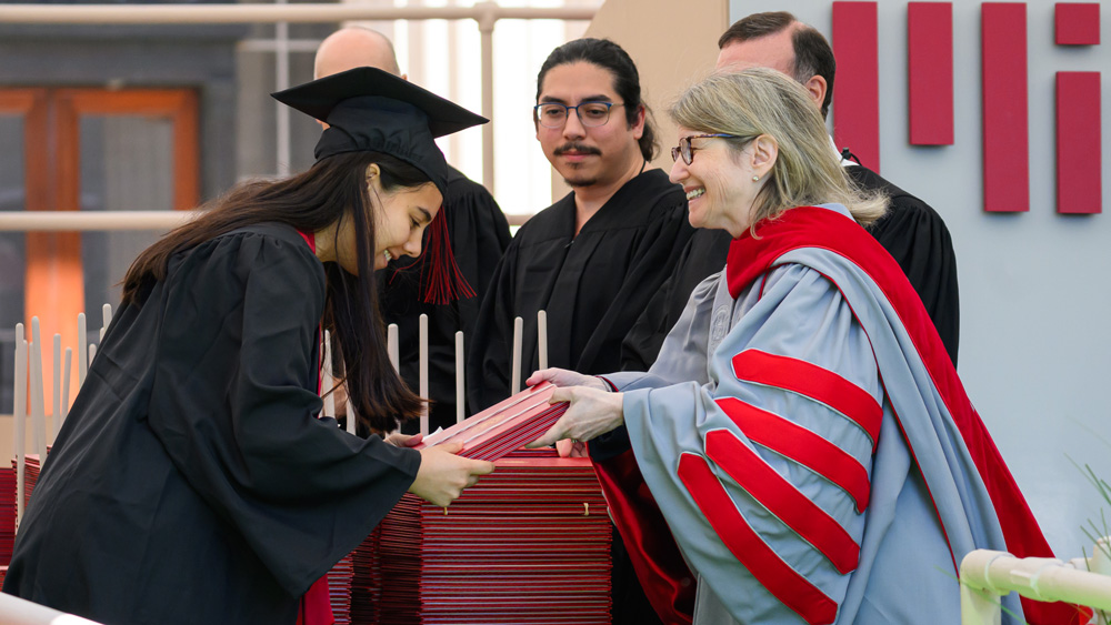Sally Kornbluth hands a graduate a diploma