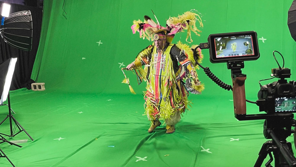 a traditionally dressed Indigenous dancer performing in front of a green screen