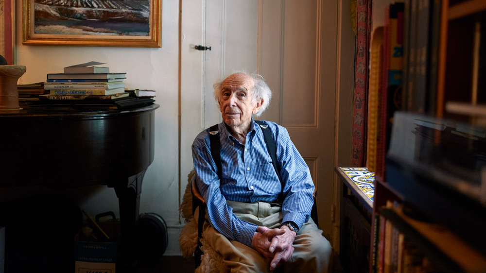 Josef Eisinger sits next to his piano and bookshelves.