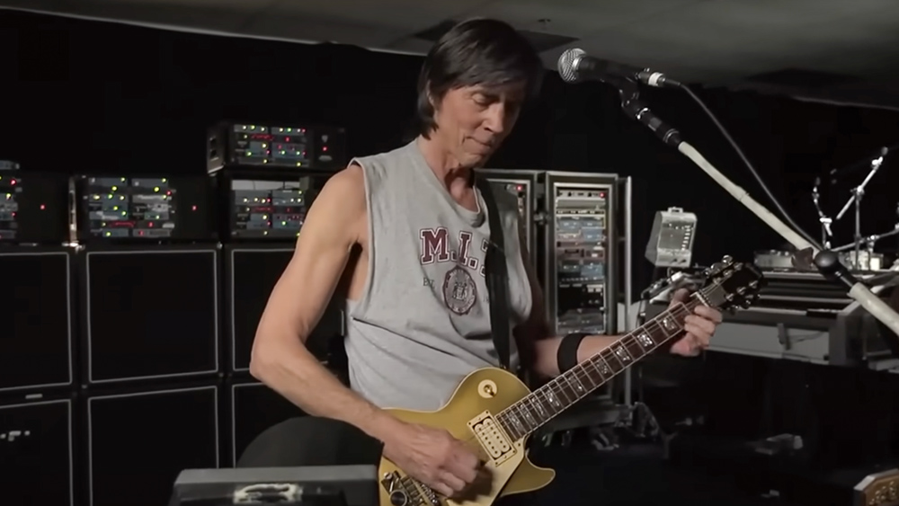 Tom Scholz plays the guitar while wearing an MIT tanktop