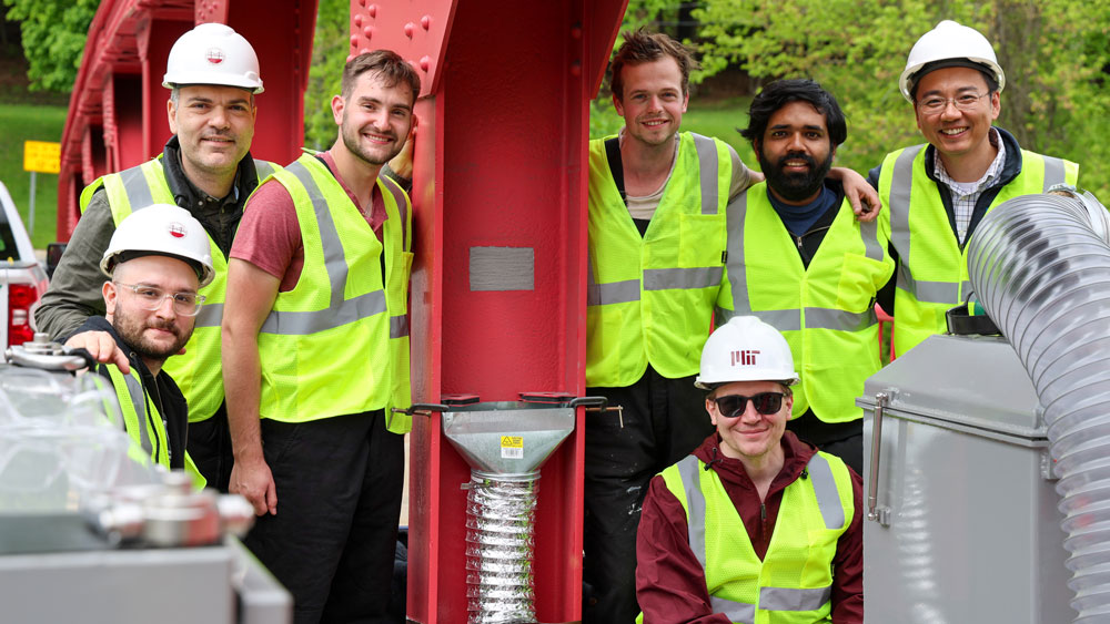 Team poses outside next to the 3D-printed patch on a red bridge.