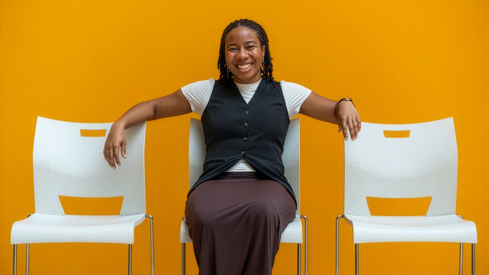 Olivia Honeycutt sits on a chair with a orange wall in background