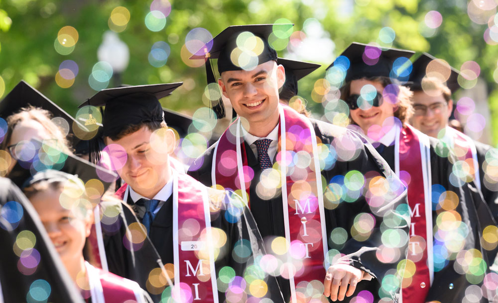 Braedon Rudolph walks with other graduates during commencement, surrounded by bubbles