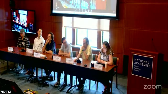 The six-person panel at the National Academies, mid-session. This discussion ran without content slides; the panelists' name placards on the table are the only on-screen text.